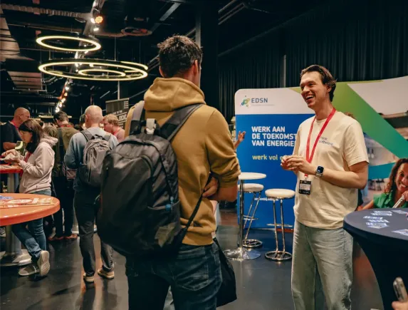 Tonny Garić in een Flink Software t-shirt staat lachend in gesprek met een bezoeker op een drukbezochte J-Spring 2025.