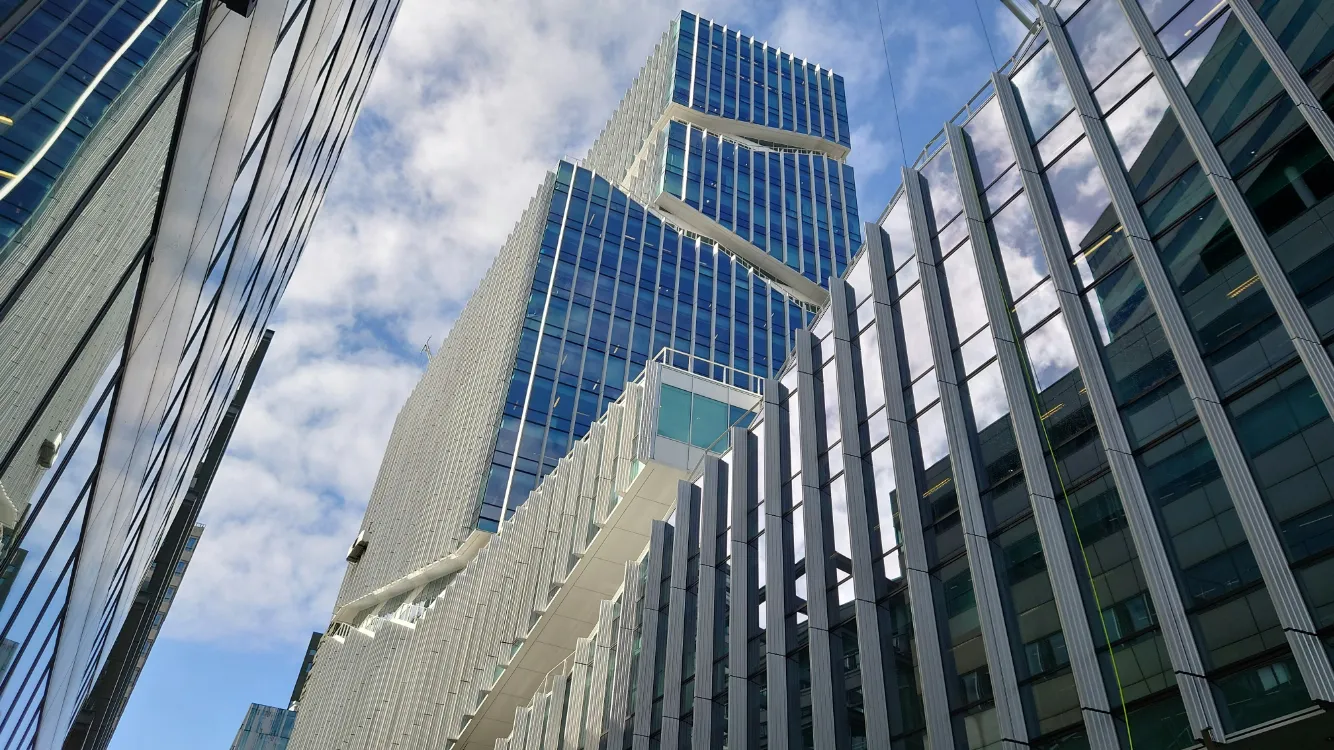 Lage-hoekfoto van moderne, glazen kantoorgebouwen die reflecteren in een blauwe lucht met wolken.